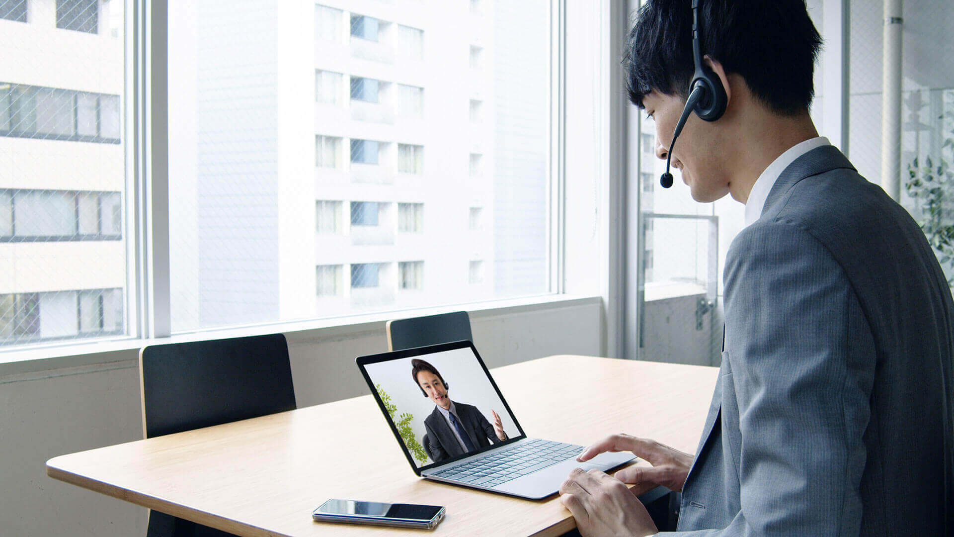 A professional conducting a telehealth session on a laptop in a modern office setting