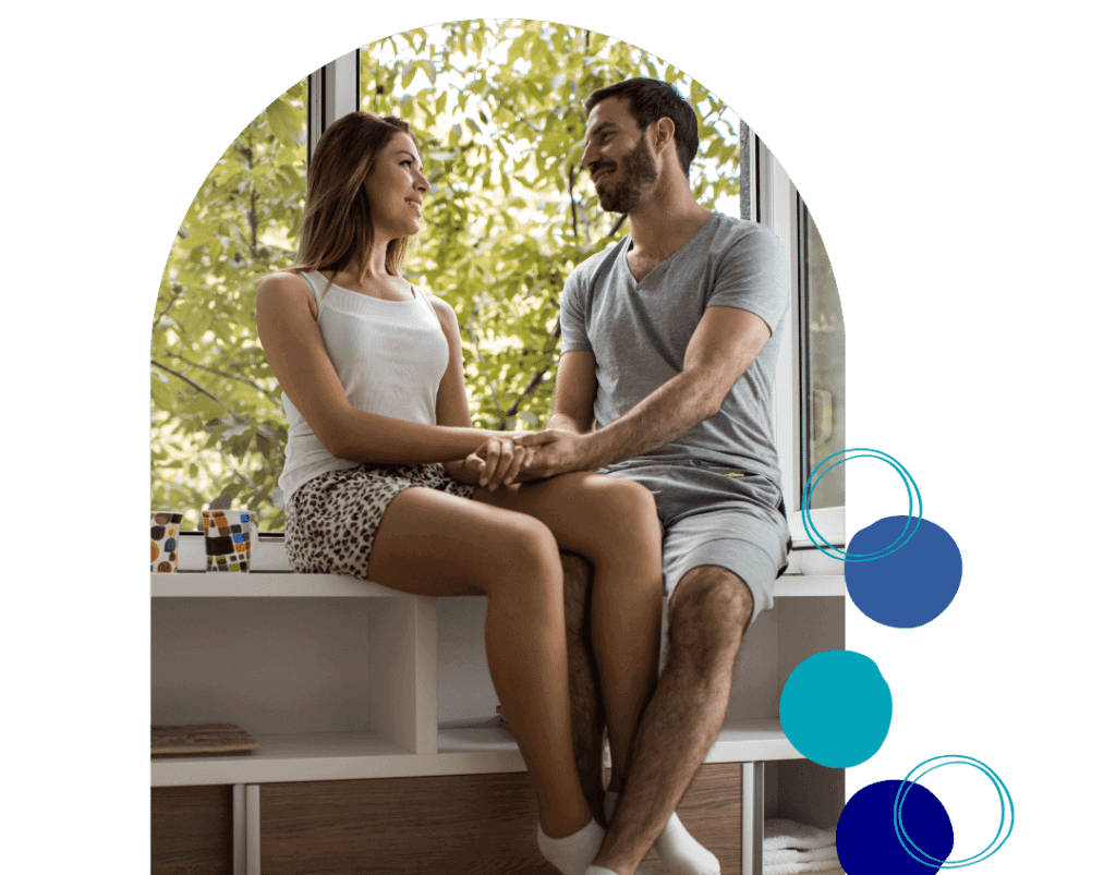 3 A happy couple sitting by a window, holding hands and smiling at each other, representing the positive outcomes of Couples Therapy in Altamonte Springs.