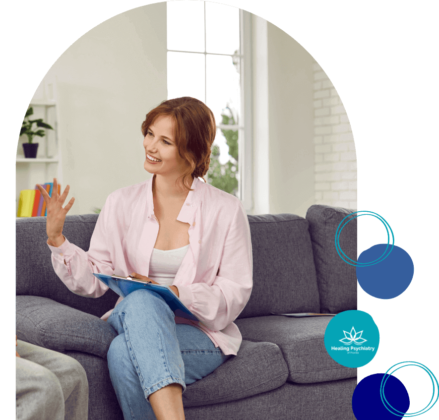 A welcoming therapist with short hair is seated comfortably on a gray sofa, clipboard in hand, engaging in a discussion, exemplifying the attentive care provided by Lake Mary Psychiatric Services.