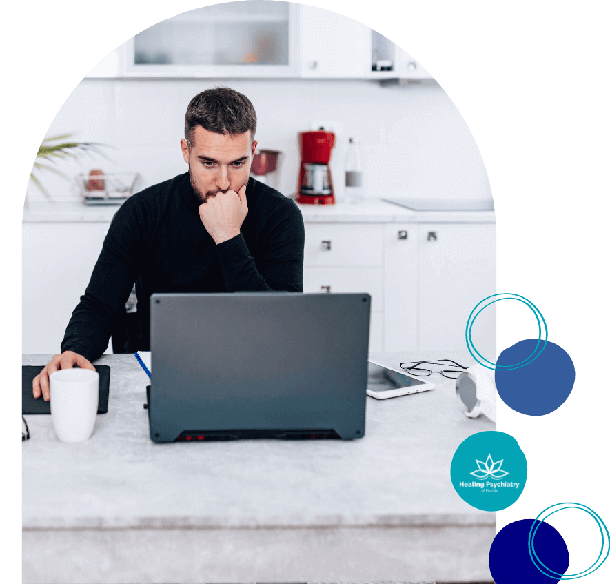 A man in deep concentration sits at a kitchen counter with a laptop and a coffee mug