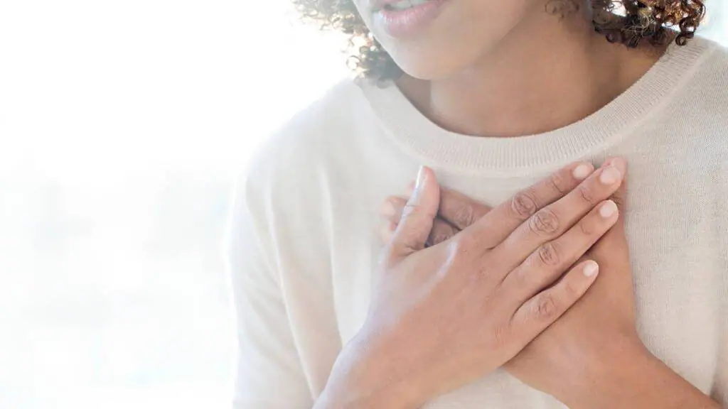 A close-up of a woman holding her hands over her chest, appearing to take deep breaths, possibly experiencing anxiety or stress