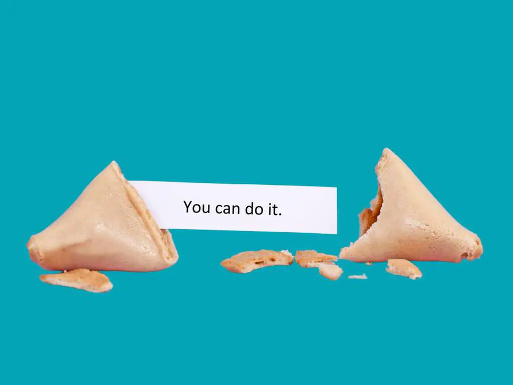 A broken fortune cookie with a slip of paper that reads "You can do it" against a turquoise background