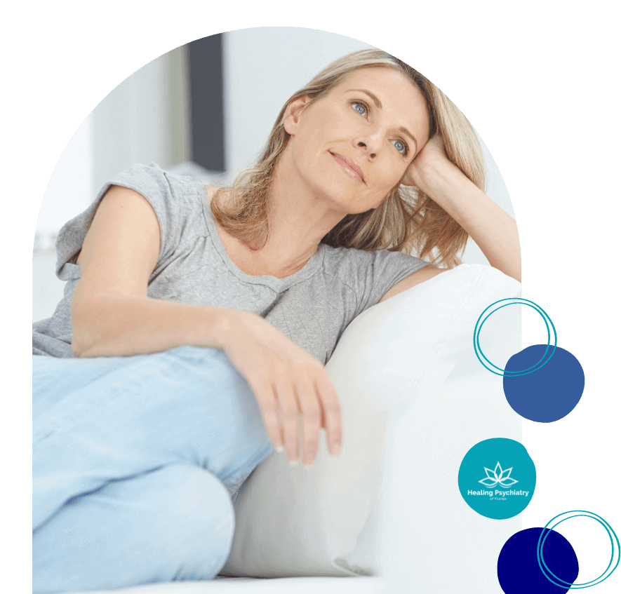 A middle-aged woman sits thoughtfully on a couch, reflecting a calm and peaceful state after receiving anxiety treatment services at Healing Psychiatry of Florida.