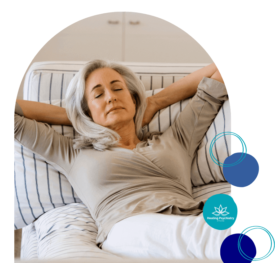 A middle-aged woman sits thoughtfully on a couch, reflecting a calm and peaceful state after receiving anxiety treatment services at Healing Psychiatry of Florida.