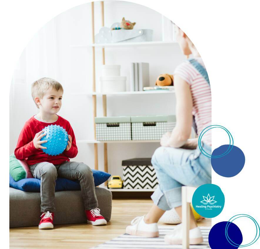 adhd kids (3) A young boy holds a blue ball while talking to a therapist during a therapy session in a bright, inviting room designed for children.