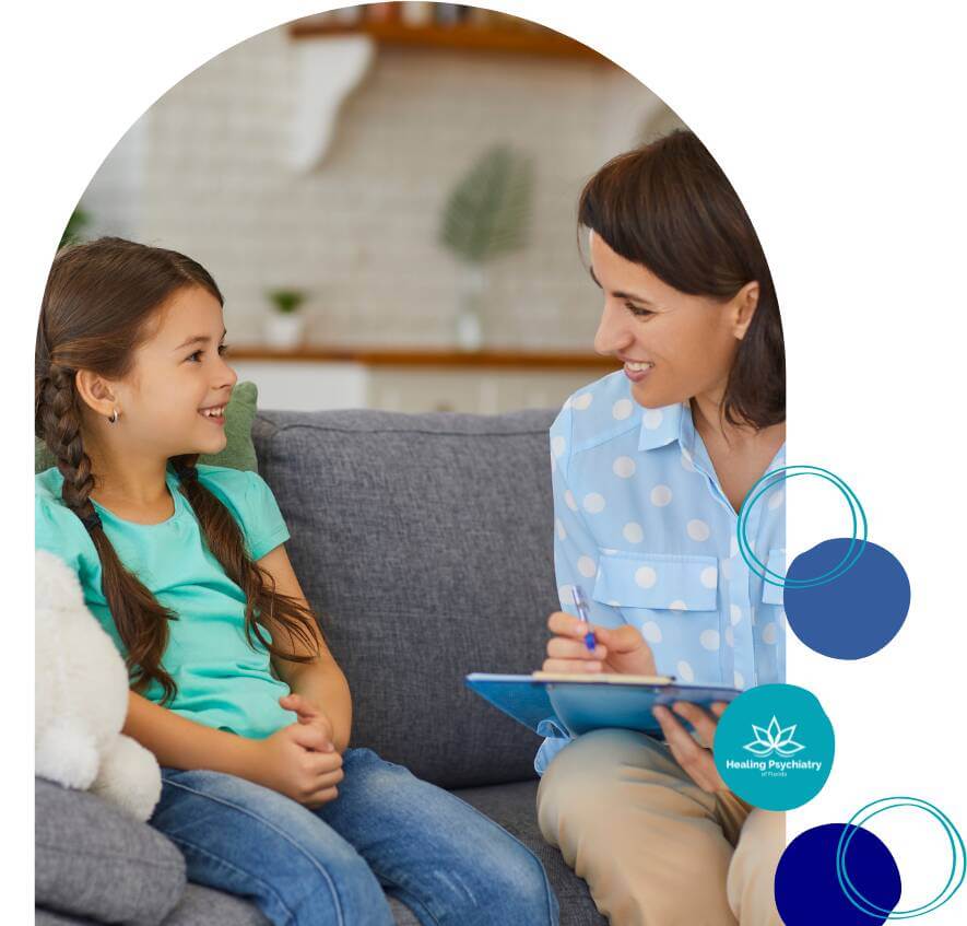 children therapy (2) A young girl smiling and talking with a female therapist who is taking notes during a child therapy session at Healing Psychiatry of Florida.