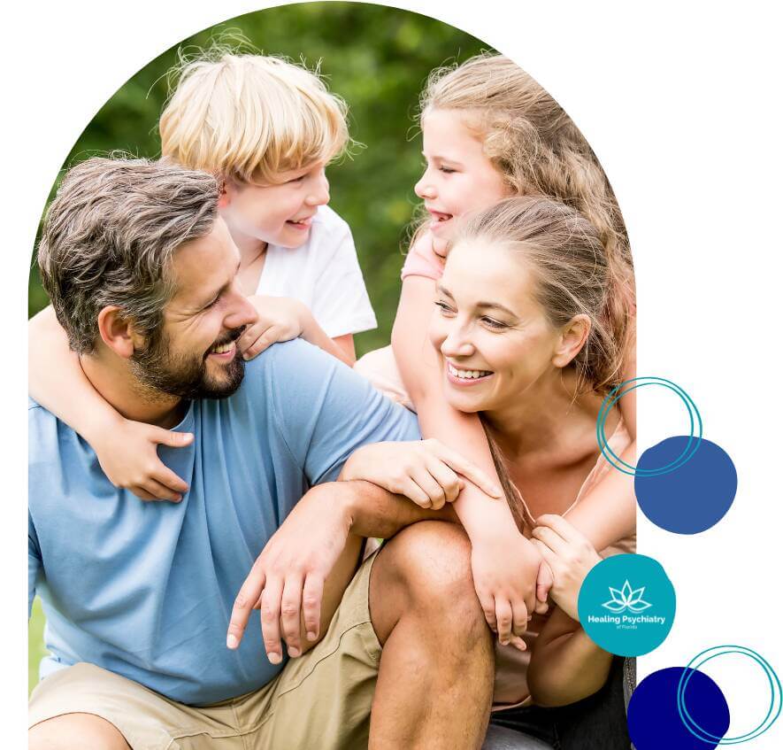 children therapy anxiety A smiling family of four enjoying a fun moment together outdoors, with two children playfully hugging their parents. The mother and father are laughing and looking at each other.