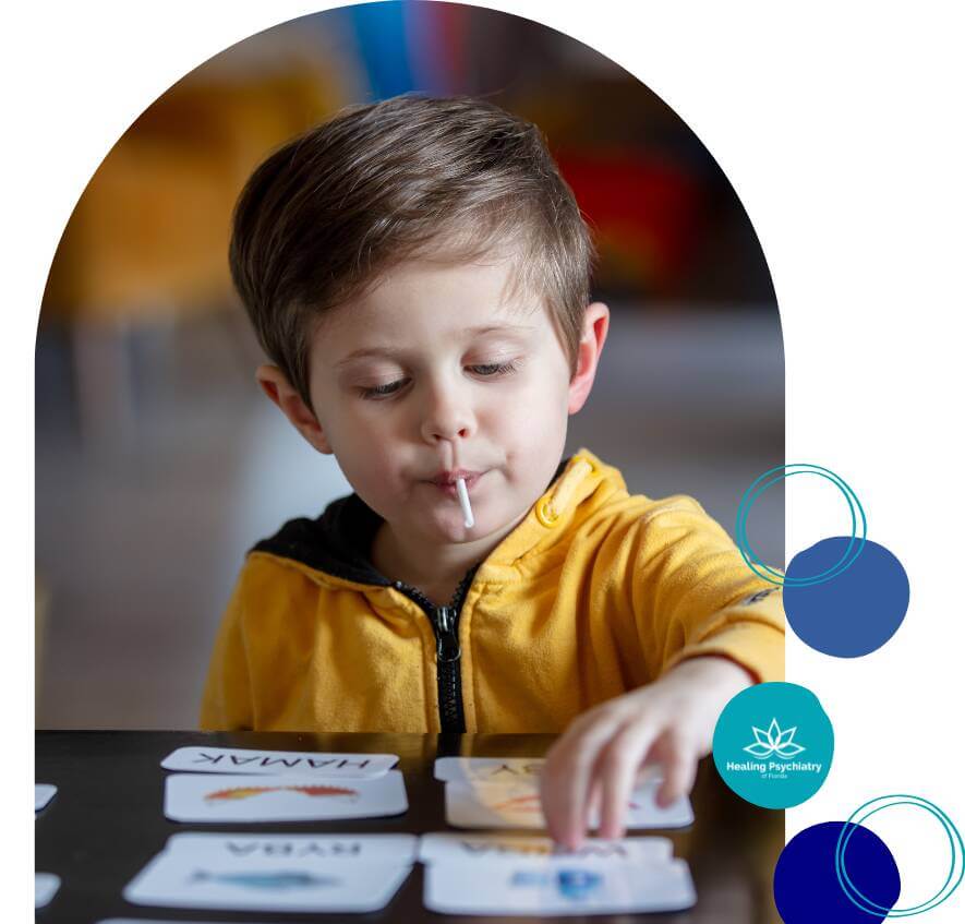 A young boy focused on matching cards during a therapy session, while enjoying a lollipop.