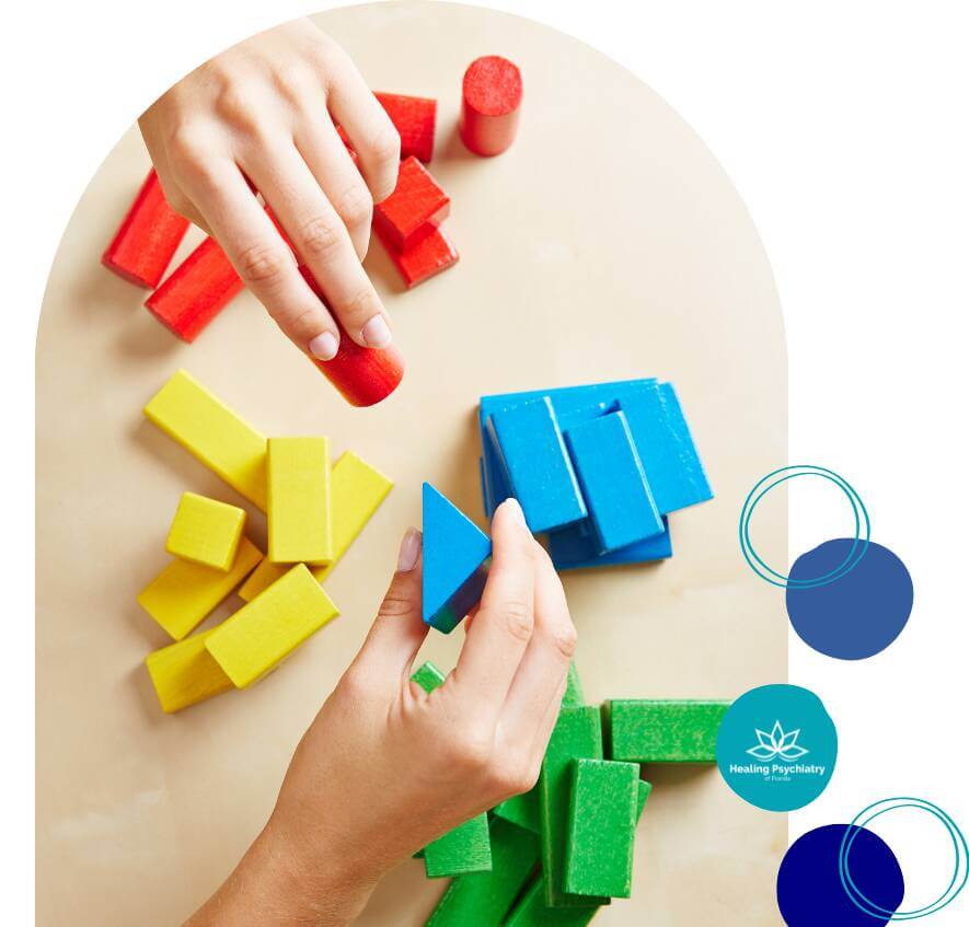 Hands arranging colorful building blocks in various shapes and colors on a table.
