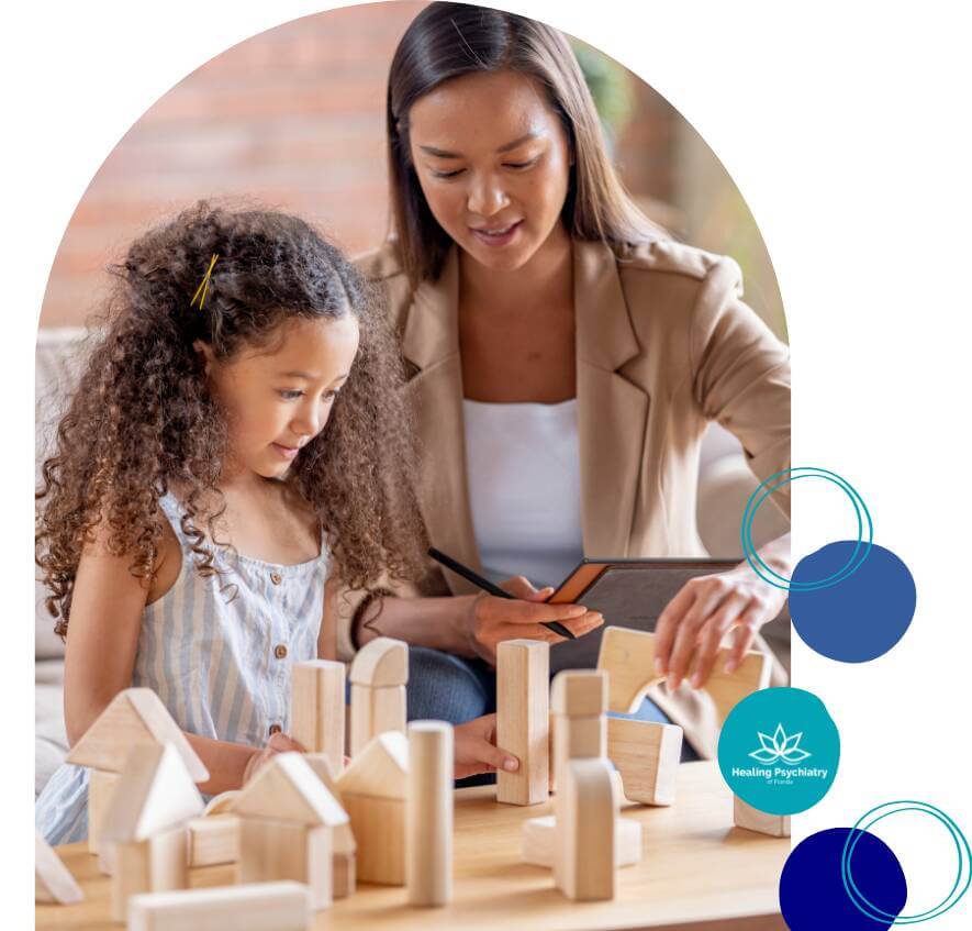 A young girl and a female therapist engage in play therapy using wooden building blocks.