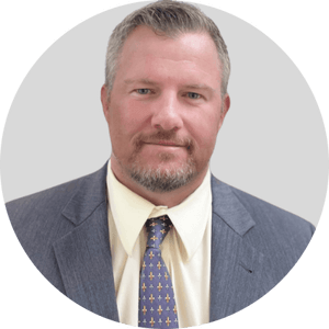 Professional headshot of Robbie Phillips, a child therapist. He has short grayish hair and a trimmed beard, and is wearing a gray suit, light yellow shirt, and a patterned tie. He is facing forward with a calm, professional expression.