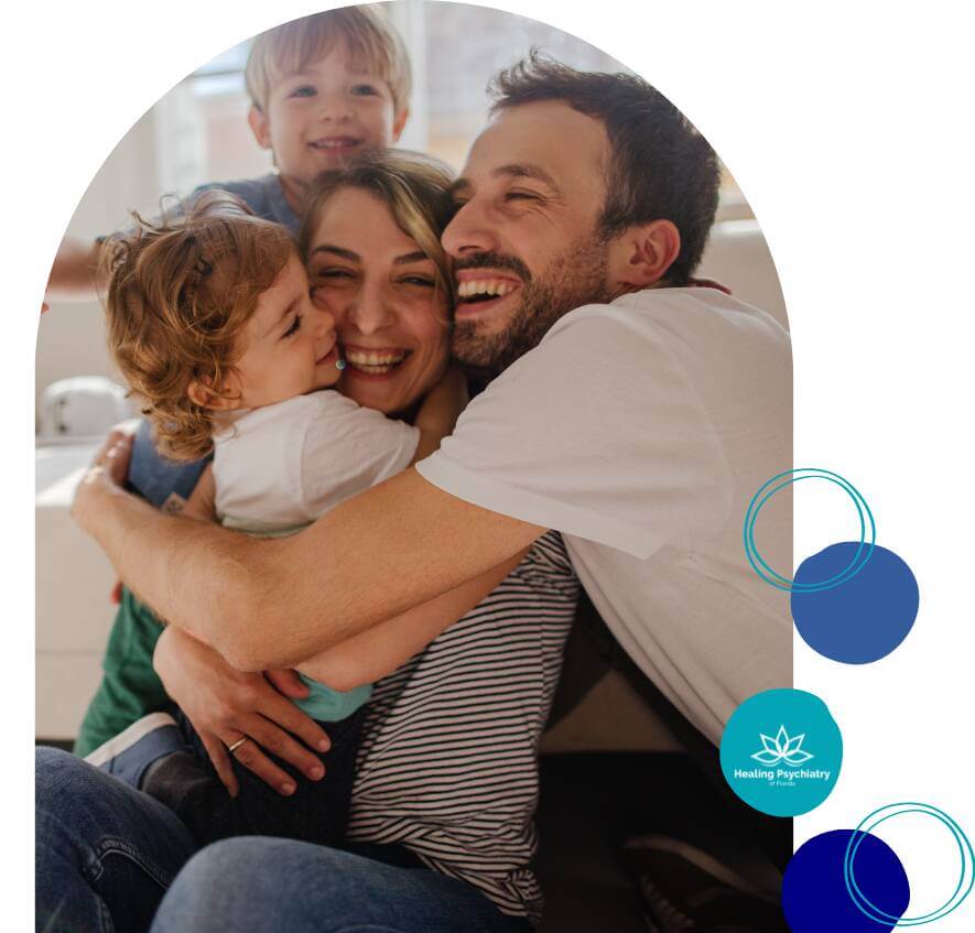 A joyful family of four shares a group hug, smiling warmly in a sunlit room.