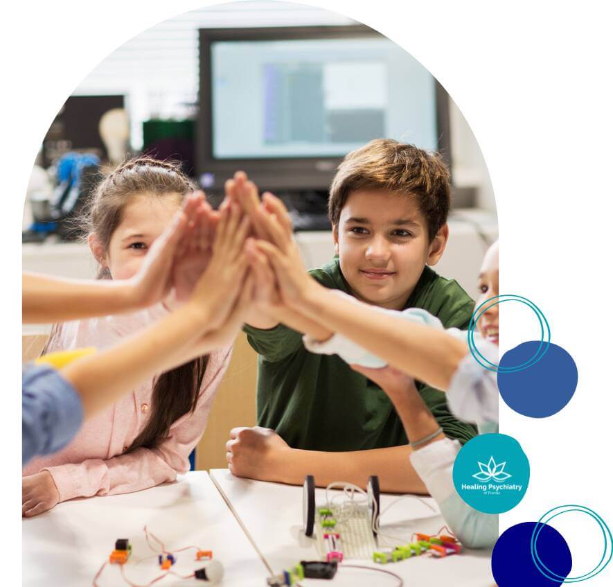emotional regulaton therapy2 A group of children smiling and high-fiving at a table during a collaborative therapy or learning activity.