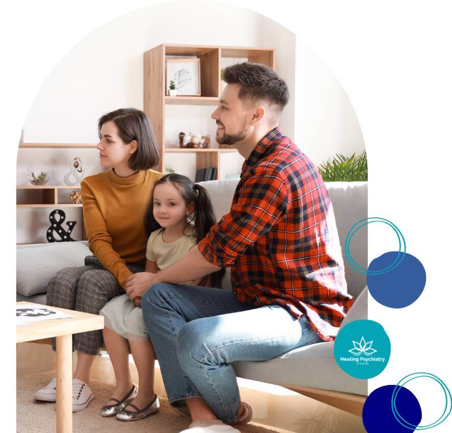 A mother, father, and young daughter sit together on a couch during a calm and supportive family therapy session.