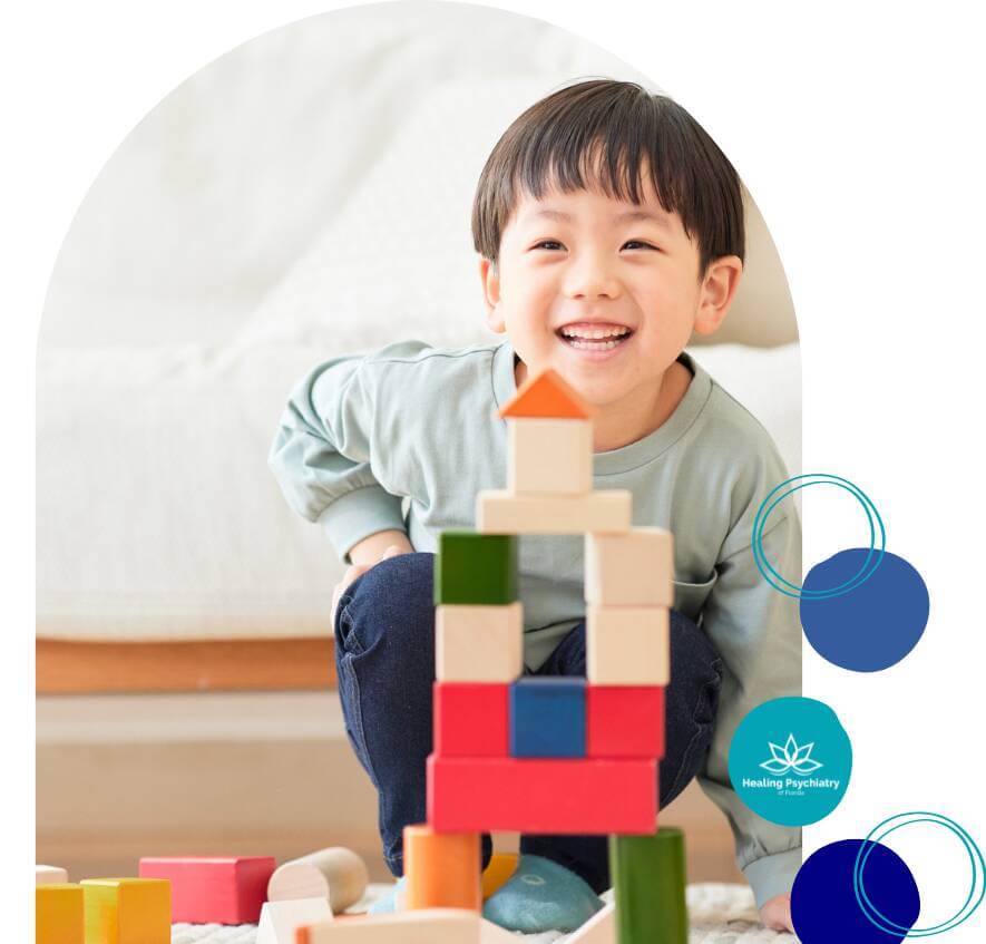 therapy for social challenge Young boy smiling while playing with colorful wooden building blocks during a therapy session at Healing Psychiatry of Florida.