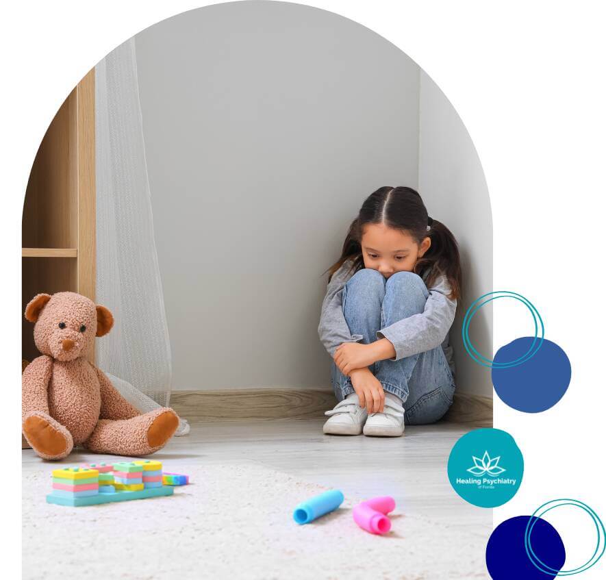 therapy for social challenge2 Sad young girl sitting alone in a corner with knees hugged to her chest, surrounded by toys and a teddy bear, symbolizing emotional distress and social withdrawal.
