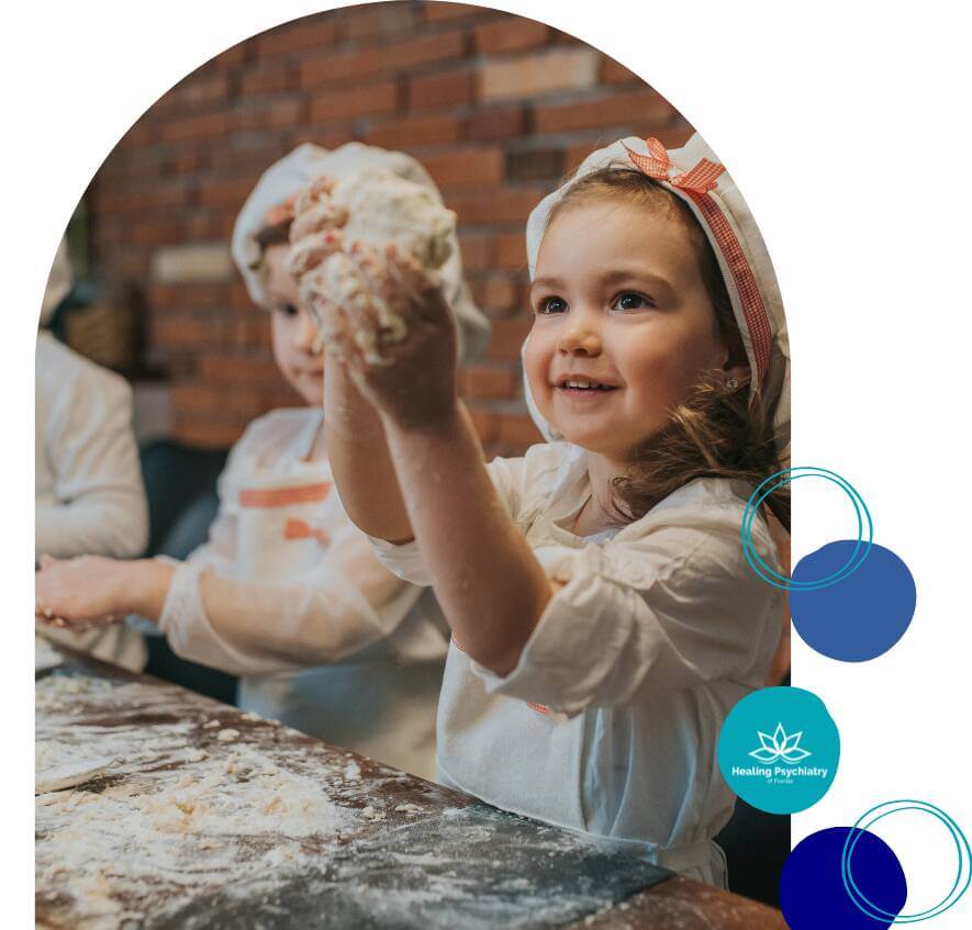 therapy for social challenge3 Young girl in a chef’s hat smiling while playing with dough during a fun and interactive group activity at Healing Psychiatry of Florida.