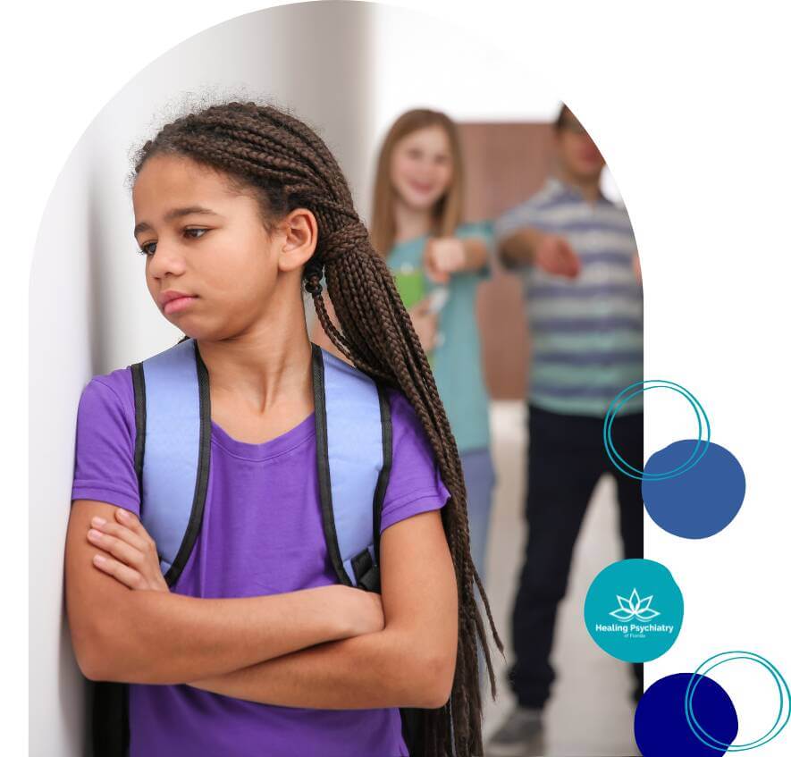A young girl with crossed arms and a backpack looks upset as two children in the background point and laugh at her.